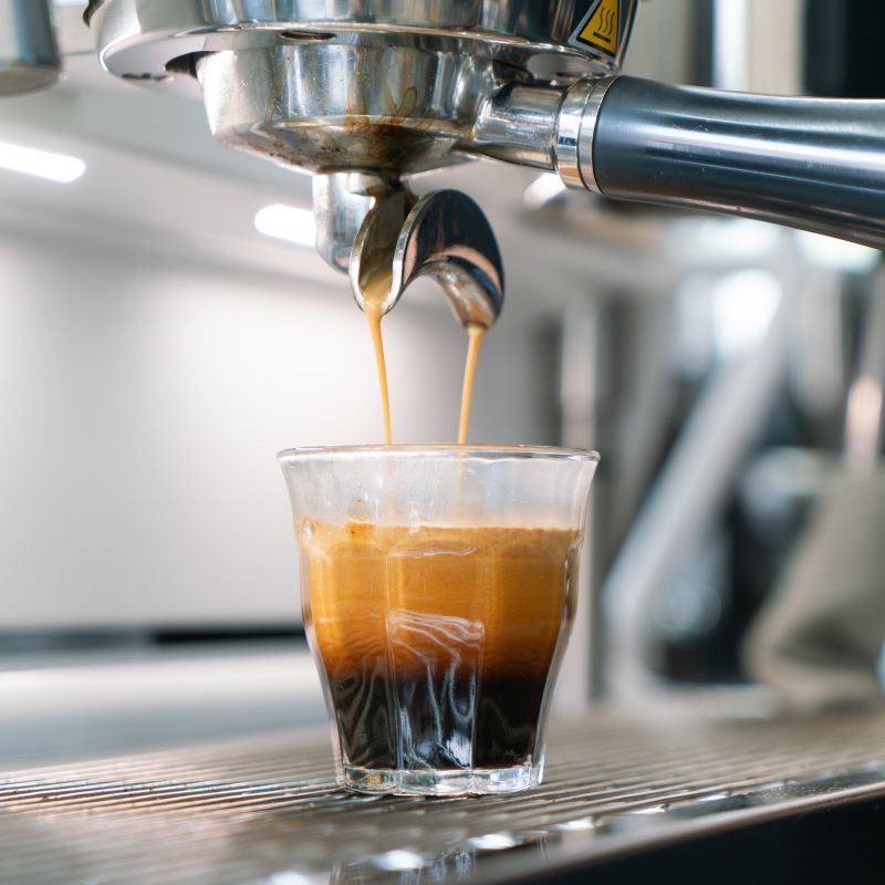Espresso being poured from a machine into a glass on a blurred background