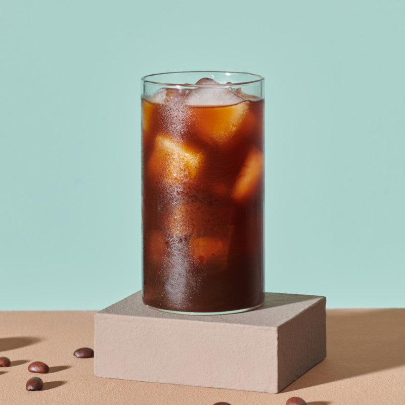 Glass of iced coffee with ice cubes on a light blue background