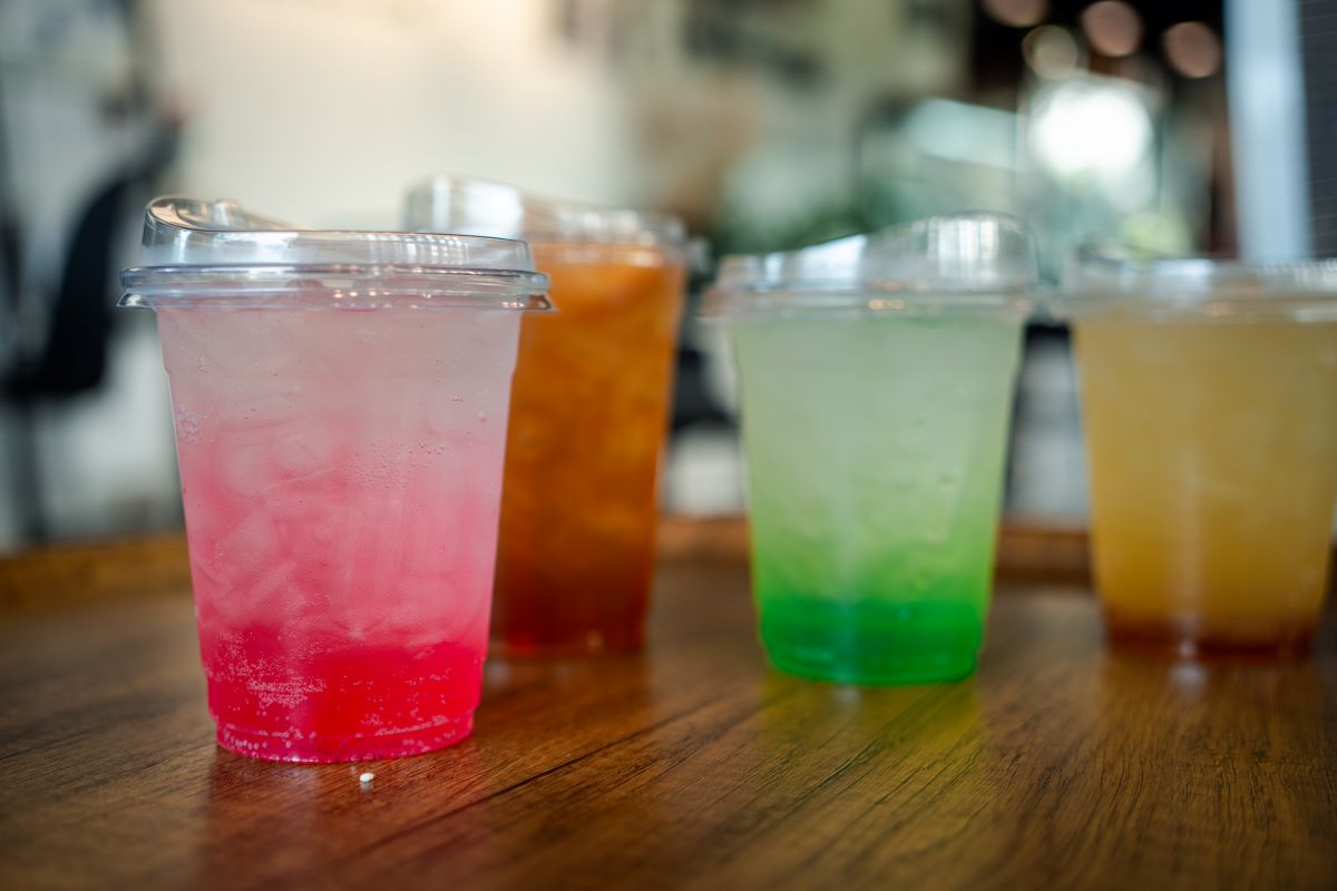Four colorful drinks in transparent cups on a wooden surface with a blurred background