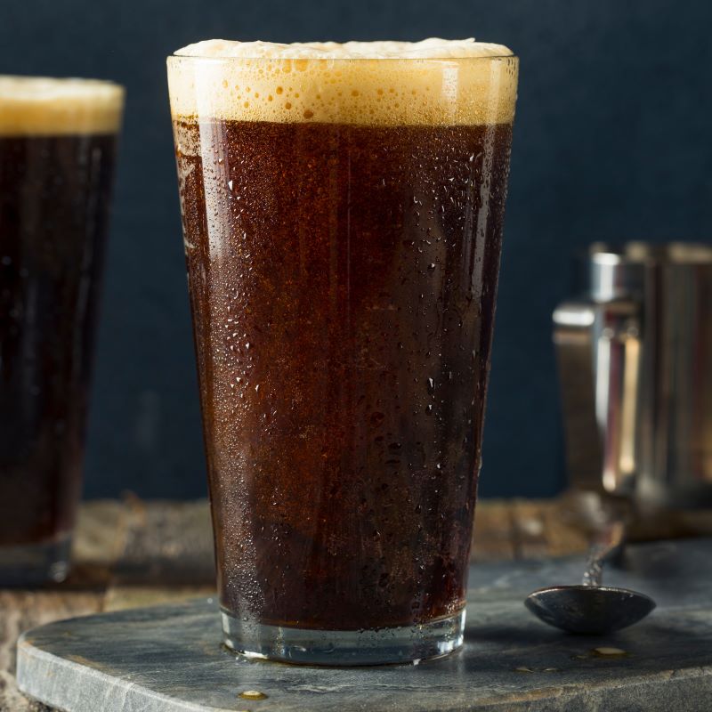 Glass of dark beer with foam on a wooden surface