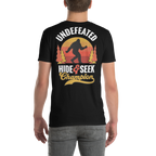 Black t-shirt with 'Undefeated Hide & Seek Champion' design featuring a silhouette of a person and trees on a white background.