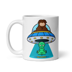 White mug with a cartoon design of a brown bear in a UFO and a green alien, on a white background.