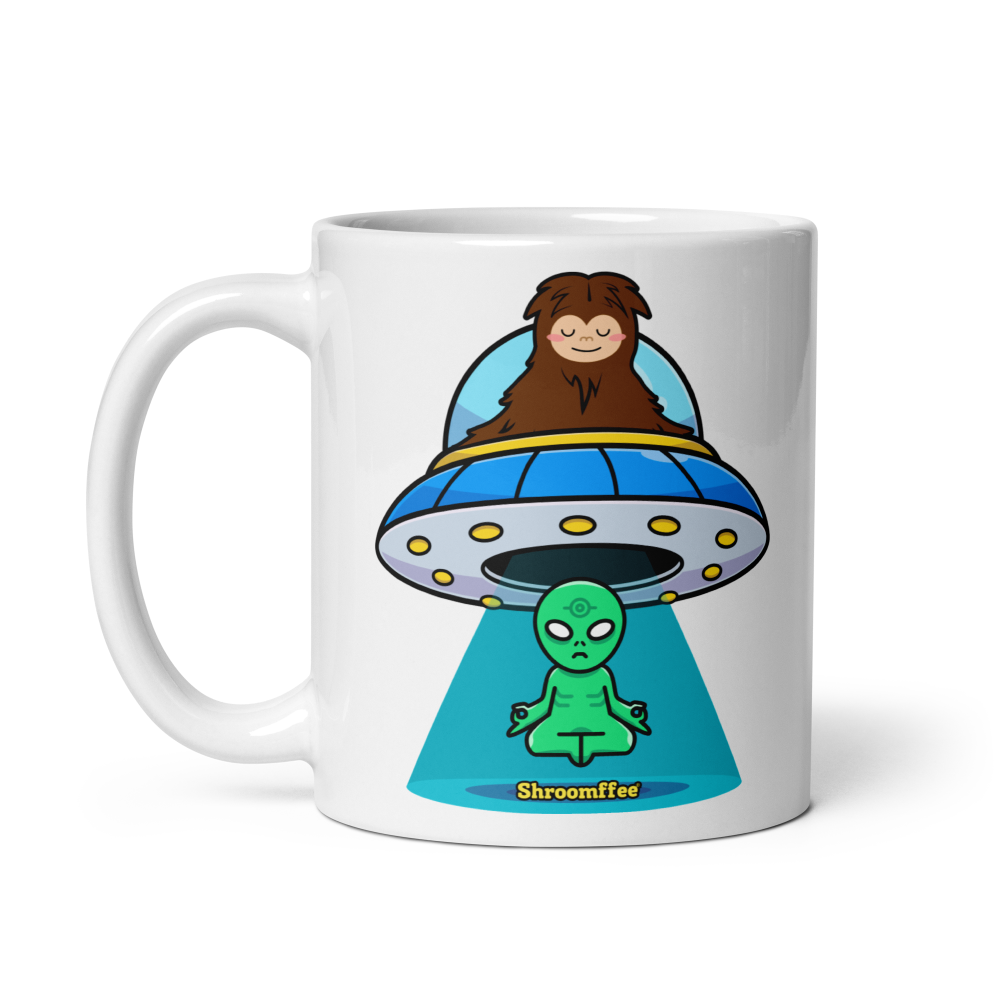 White mug with a cartoon design of a brown bear in a UFO and a green alien, on a white background.