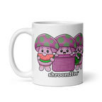A white ceramic mug with cartoonish mushroom characters in pink and purple colors, with the word 'shroomies' written on it.