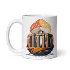 A white ceramic mug with a fantasy illustration of mushrooms growing atop a stone structure reminiscent of ancient architecture.